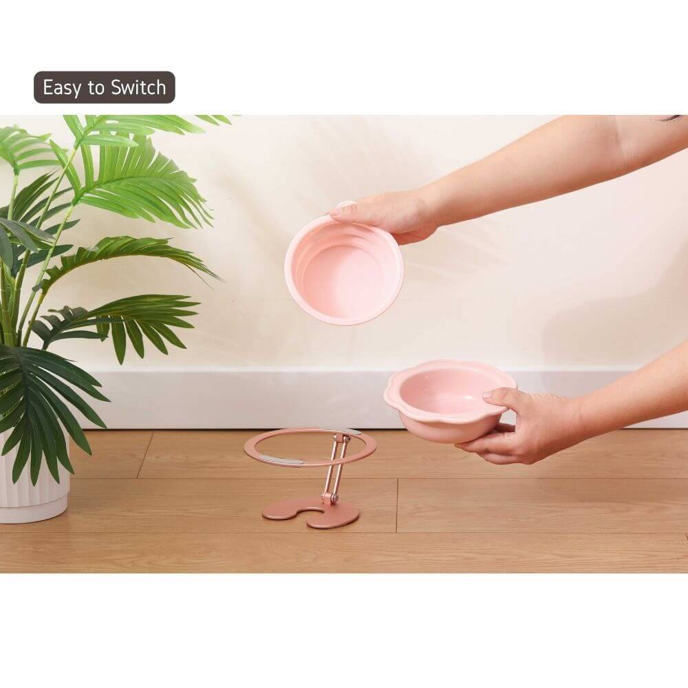 Person adjusting a modern pink pet bowl on a multi-angle adjustable pet bowl stand with green plant in the background.