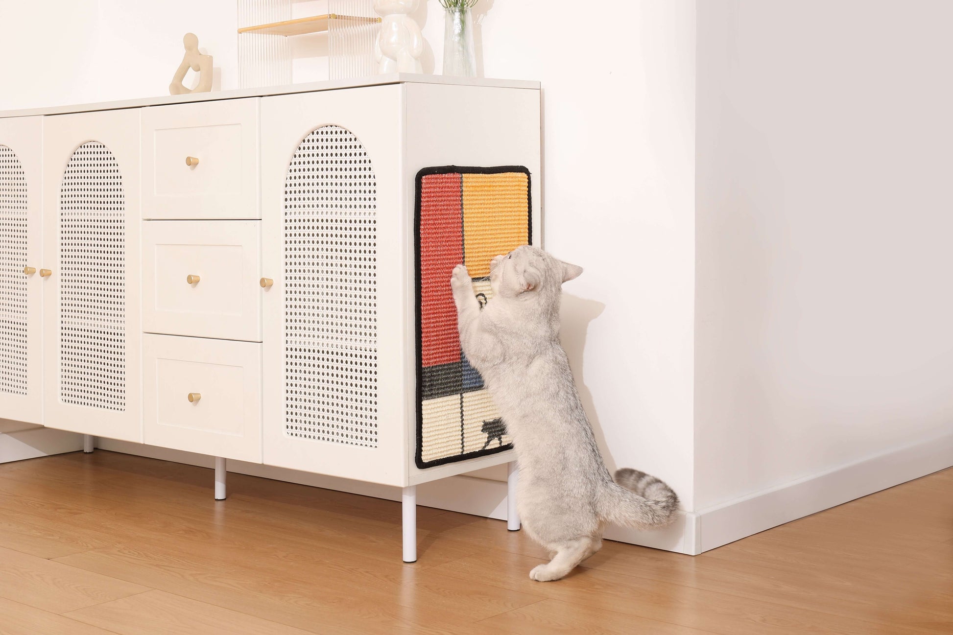 Cat using an art-inspired natural sisal scratching mat on a cabinet, promoting safe scratching and play.