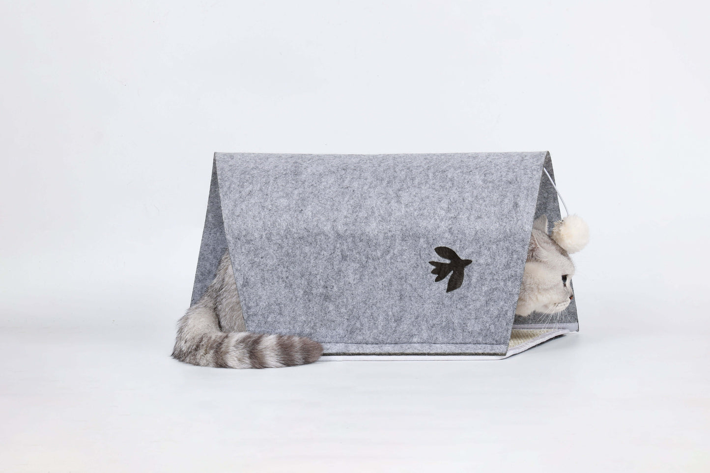 Cat playing in a modular felt tunnel with bird-shaped peephole and pom-pom toy, featuring a scratch-friendly design for interactive fun.